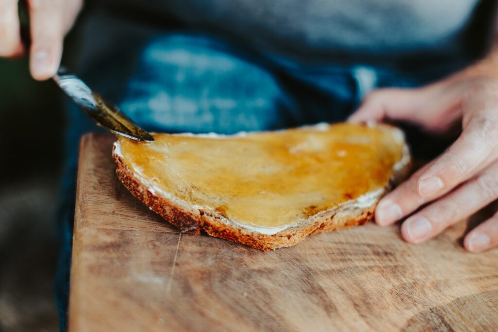 Cremiger Honig wird mit dem Messer auf eine Scheibe Brot gestrichen