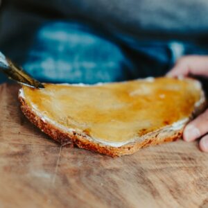 Cremiger Honig wird mit dem Messer auf eine Scheibe Brot gestrichen