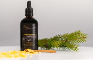 Propolis Tropfen 40 % in der 100-ml-Flasche mit Pipette, daneben Bienenwachs und Holzlöffel